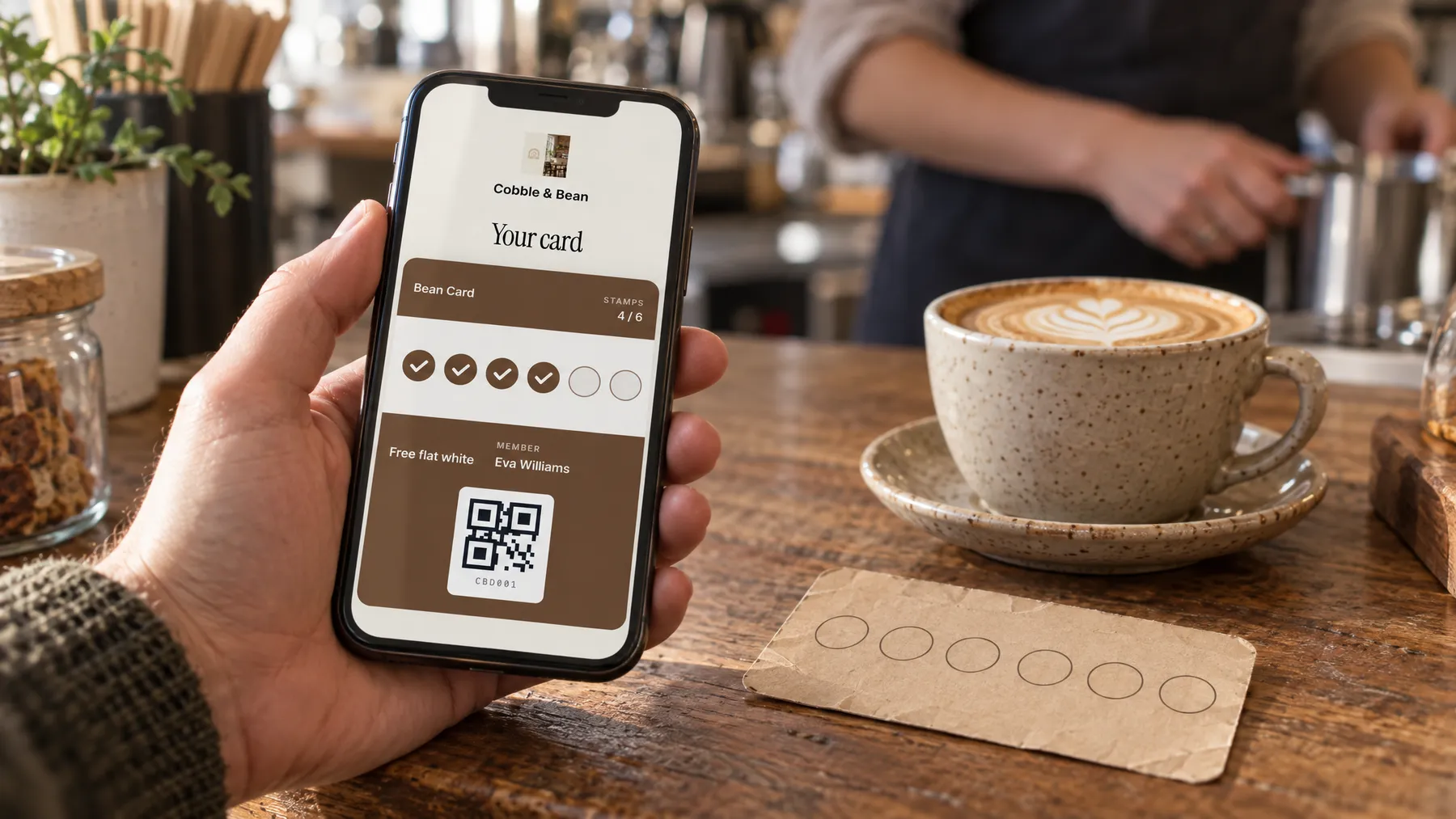 A phone showing a digital stamp card next to a paper stamp card and a flat white on a café table