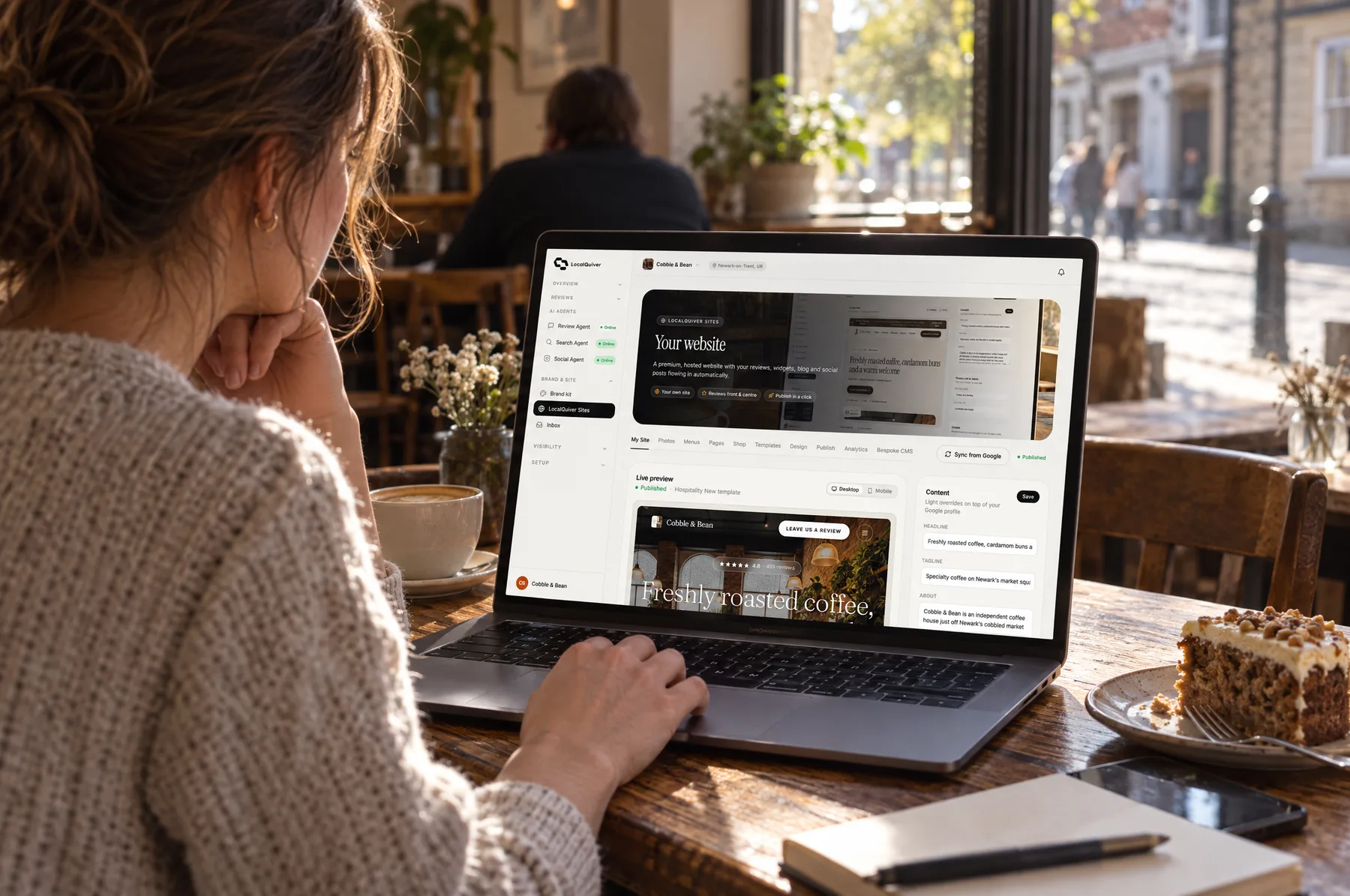 Someone at a café table editing a website in LocalQuiver Sites on a laptop, a coffee beside them