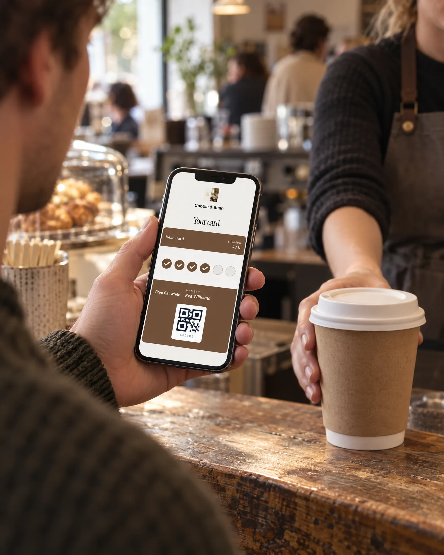 A customer holding a phone showing a digital stamp card at a café counter